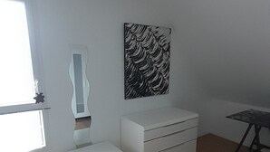 Una habitació amb una banca blanca, un armari blanc, una obra d'art en blanc i negre a la paret i una finestra.