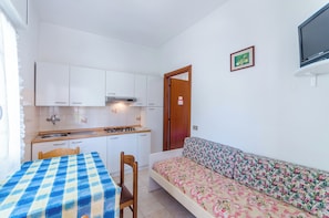 A compact kitchen with white cabinets, a wooden table, and a sofa with a floral cover. - Flat a Short Walk to the Beach (San Michele al Tagliamento)