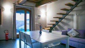 Un coin repas avec une table et des chaises, un canapé violet, un escalier et une vue à travers une porte.
