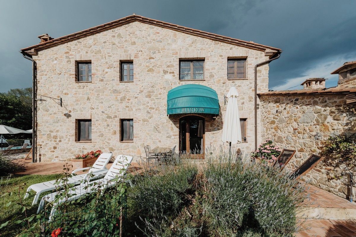 Un edificio in pietra con un ingresso centrale, una zona coperta e posti a sedere all'aperto.