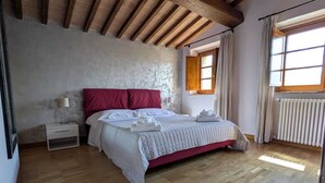 Une chambre avec un plafond en bois, un lit avec une literie rouge et blanche, une table de chevet, une fenêtre avec des rideaux et un radiateur.