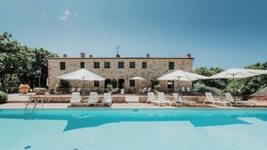 Un bâtiment en pierre doté d’une piscine, de chaises longues blanches et de parasols.