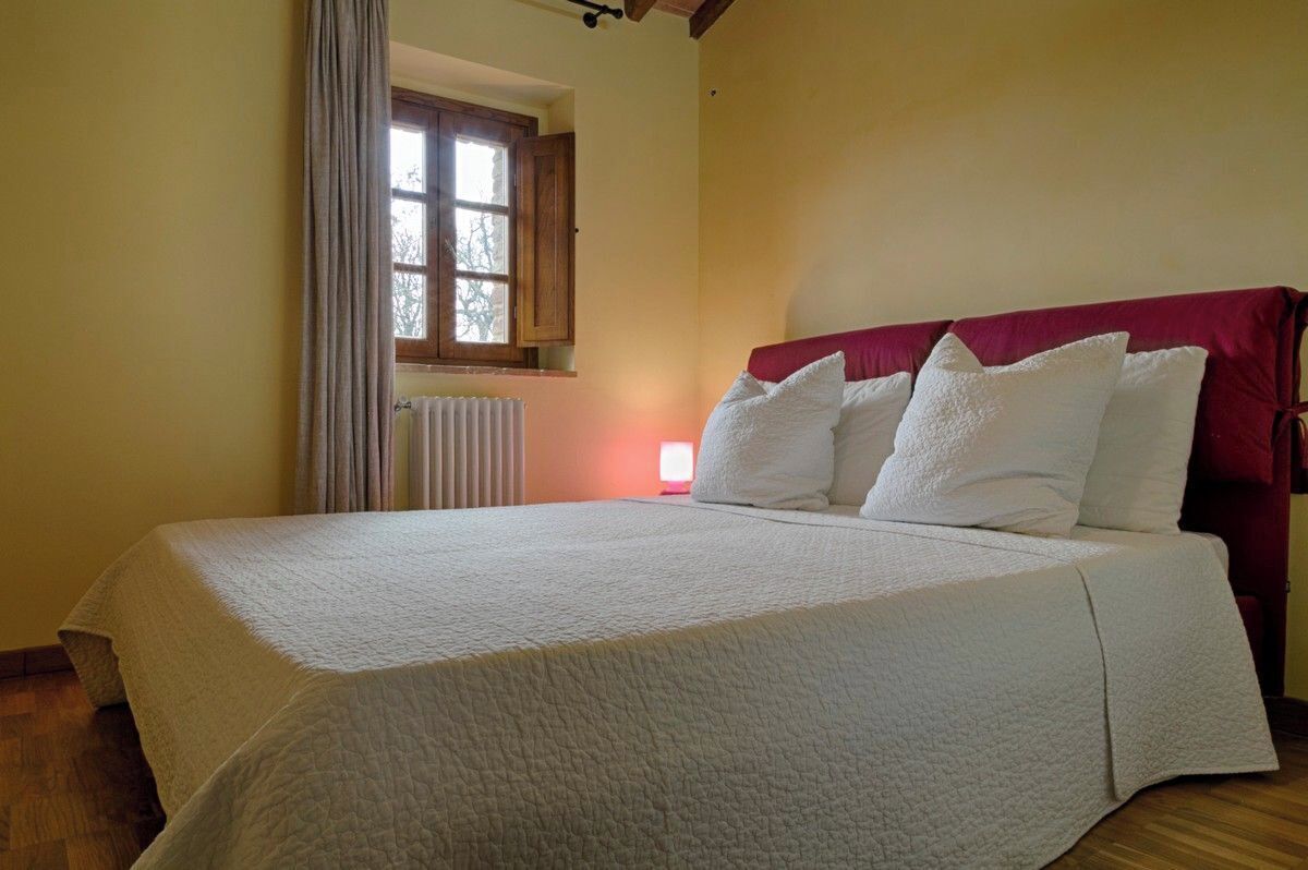 A bedroom with a large bed, a window with curtains, a radiator, and a red headboard.