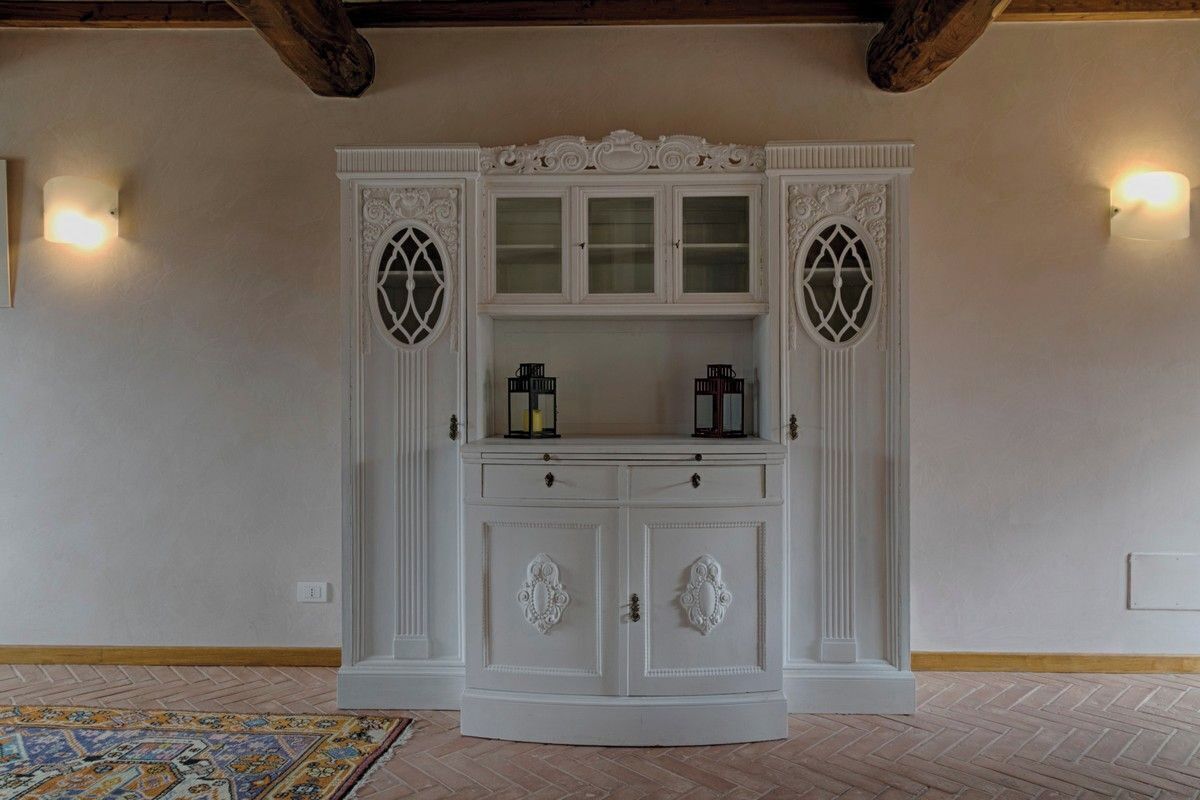 Un mobile bianco decorato con ante in vetro e due pannelli laterali, un tappeto a motivi sul pavimento e due applique a parete.