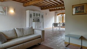 A room with a herringbone-patterned floor, a white sofa, a wooden ceiling, and a dining area with a table and chairs. - Four-room flat 6/8 sleeps Nr 4 (Cornocchia)