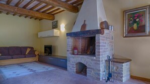 A living room with a stone fireplace, wooden ceiling beams, a sofa, and a painting on the wall. - Four-room flat 6/8 sleeps Nr 4 (Cornocchia)