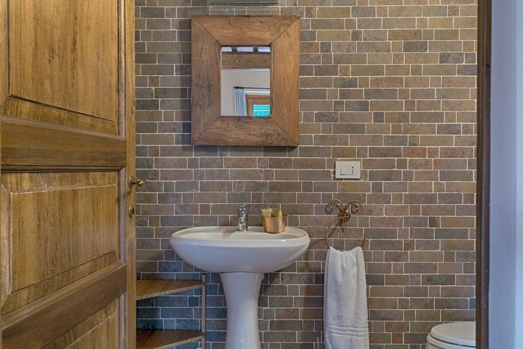 A bathroom with a wooden door, a white pedestal sink, a mirror with a wooden frame, and a towel rack.