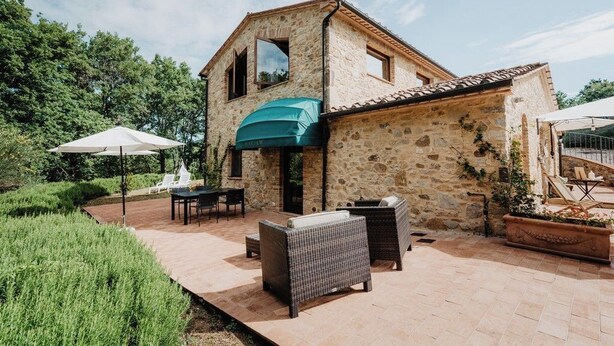 Un edificio de piedra con un patio cubierto que incluye mobiliario y sombrillas.