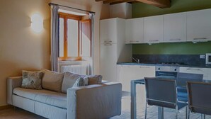 Una cocina moderna con armarios blancos, un comedor con mesa y sillas, y una sala de estar acogedora con sofá y ventana con cortinas.