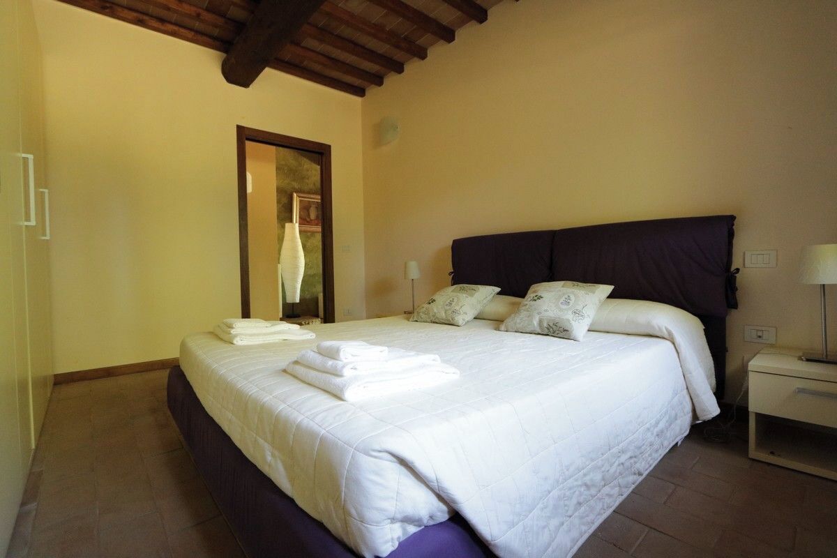 A neatly made bed with white linens and folded towels, a dark headboard, and a bedside table with a lamp.