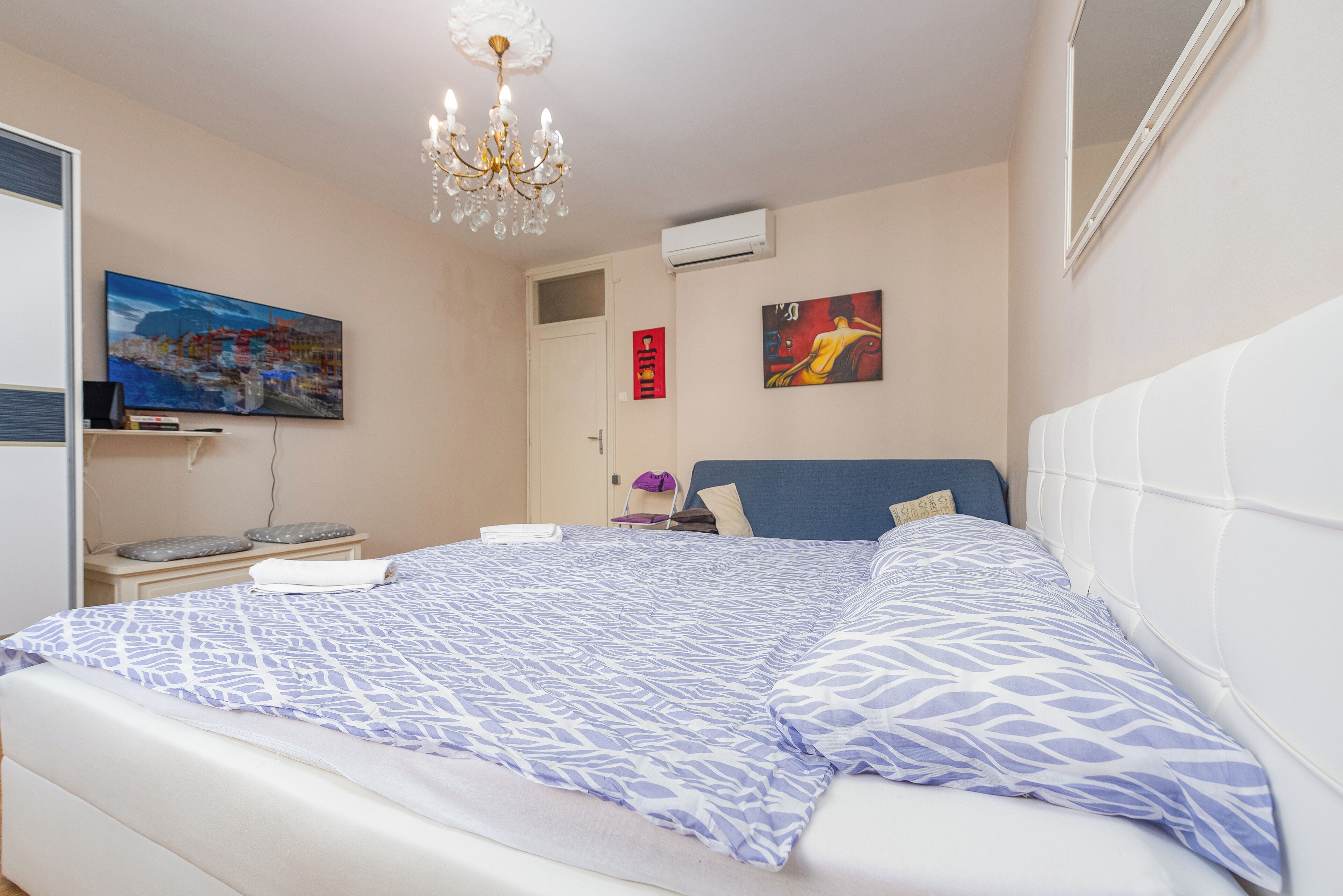 Quarto com cama grande, lustre, televisão de tela plana e obras de arte nas paredes.