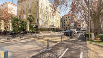 Una calle con edificios, un paso de peatones y mesas al aire libre.