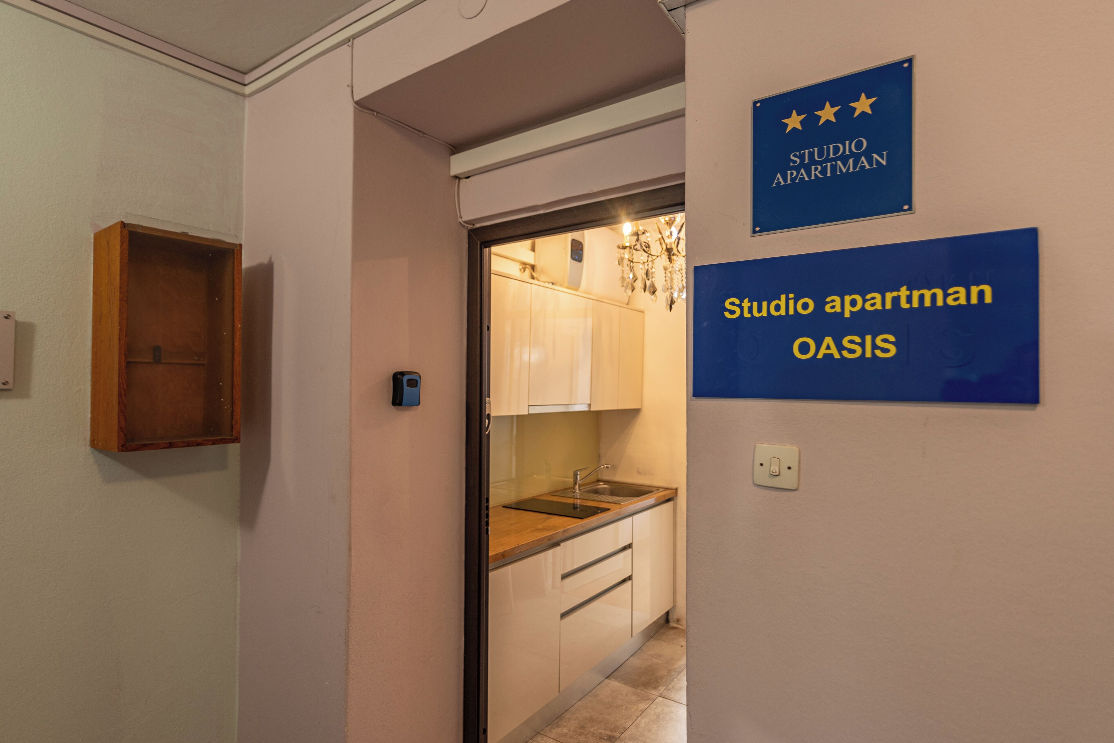 A hallway leading to a kitchen with a sink and cabinets. There are signs indicating 'Studio Apartman OASIS' and a star rating.