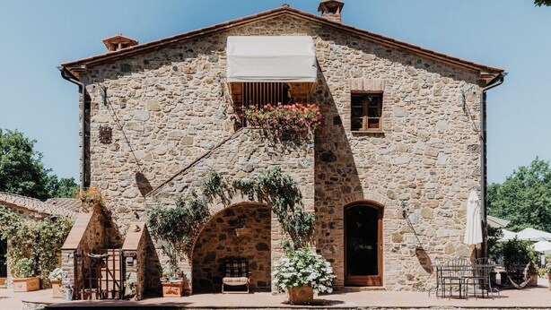 A stone building with a central archway, a small balcony with a white awning, and outdoor seating. - Standard two-room flat Nr 3 (Radicondoli)