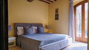 A bedroom with a large bed, two bedside tables, a wooden ceiling, and a door leading to an outdoor area. - Standard two-room flat Nr 3 (Radicondoli)
