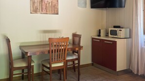 A dining area with a wooden table and chairs, a flat-screen TV mounted on the wall, and a microwave on a cabinet. - Standard two-room flat Nr 3 (Radicondoli)
