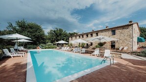 A rectangular swimming pool with white lounge chairs and umbrellas, surrounded by a stone building. - Standard two-room flat Nr 3 (Radicondoli)