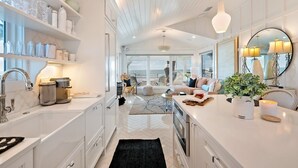 A modern kitchen with white cabinetry, a large island, and a view to the living area. - 2216 Gulf Dr 1 Bedroom Home (Bradenton Beach)