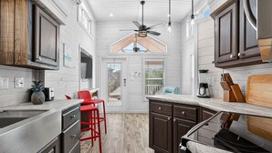 A kitchen with wooden cabinets, a red chair, and a ceiling fan. - Sailfish Rv Resort 2 Home (Port Aransas)