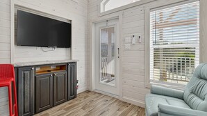 A room with a TV mounted on the wall, a wooden cabinet, a red chair, and a blue sofa. - Sailfish Rv Resort 2 Home (Port Aransas)