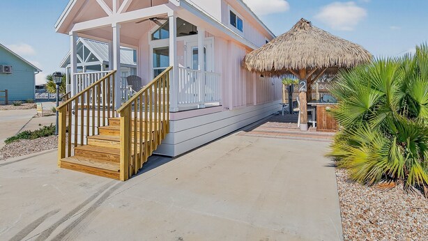 A beach house with a covered porch, a wooden staircase, and a thatched roof structure. - Sailfish Rv Resort 2 Home (Port Aransas)