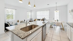 Cozinha moderna com bancada de granito, pia de aço inoxidável e iluminação pendente.