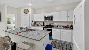 A modern kitchen with white cabinets, a granite countertop, a microwave, an oven, and a refrigerator. - Arizona Vacation Home 3 Bedroom Home (Maricopa)