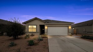 A single-story house with a garage, a driveway, and a landscaped garden with various plants. - Arizona Vacation Home 3 Bedroom Home (Maricopa)