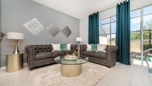 A living room with a grey sofa, two lamps, a glass coffee table, and decorative wall art. - Windsor Hills 3 Bedroom Private Pool Townhome 3 Townhouse (Kissimmee)