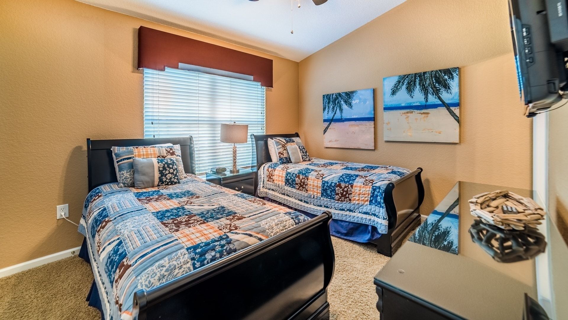 A bedroom with two beds, a desk, and artwork on the wall.