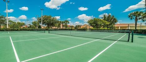 A tennis court with a net, surrounded by trees and buildings.