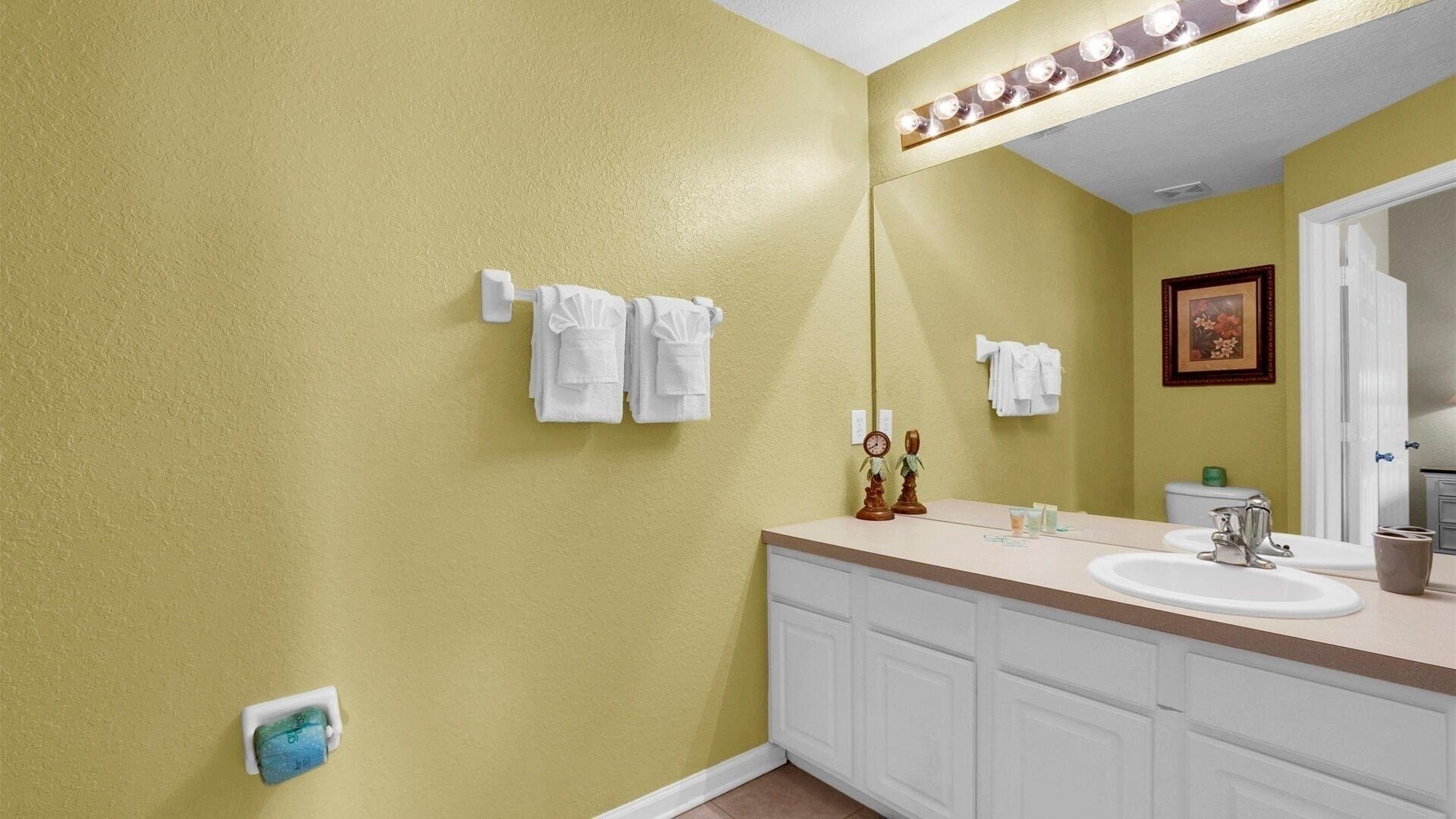 A bathroom with yellow walls, white cabinets, a sink, and a mirror with lights.