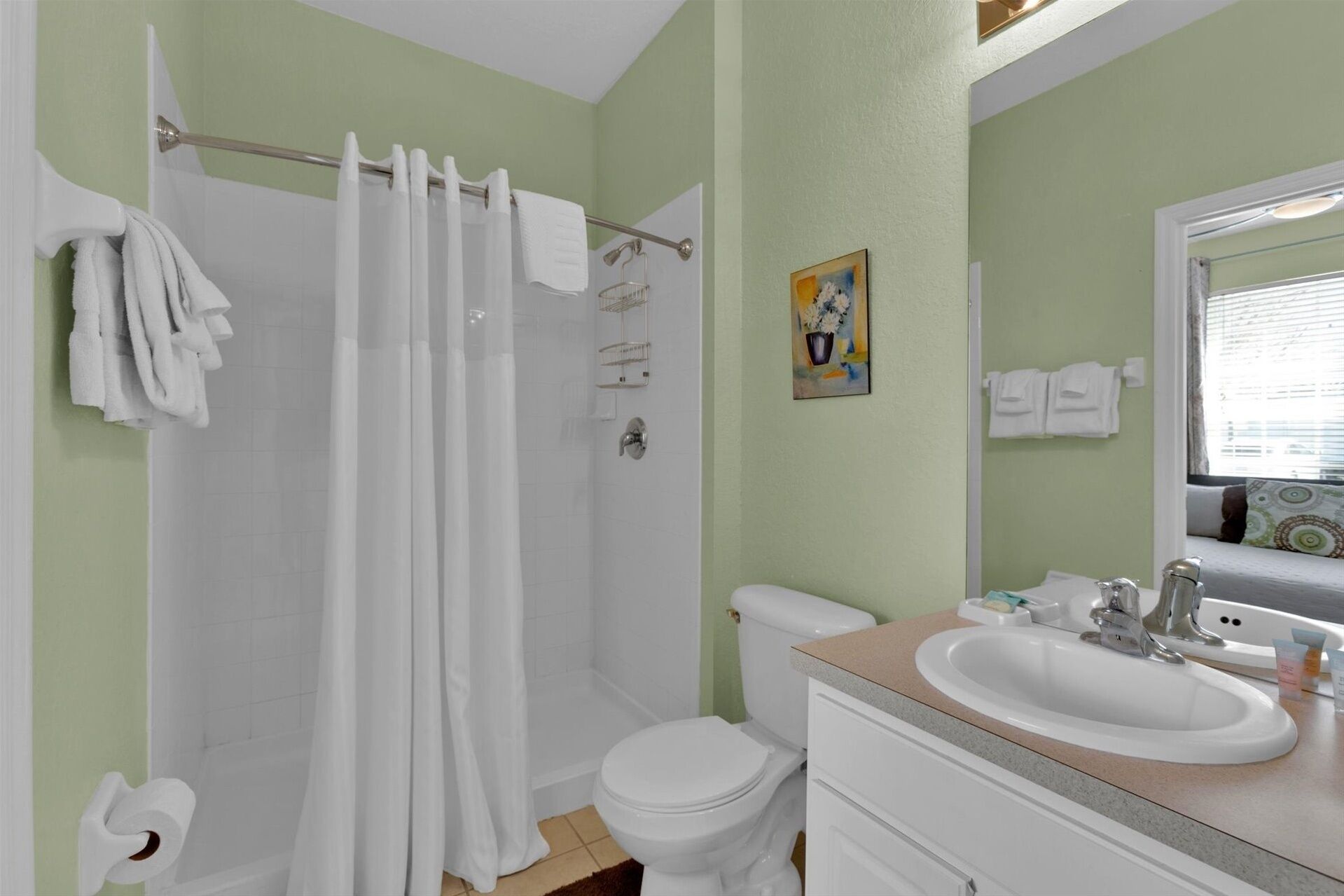 A bathroom with a shower curtain, toilet, sink, and a painting on the wall.