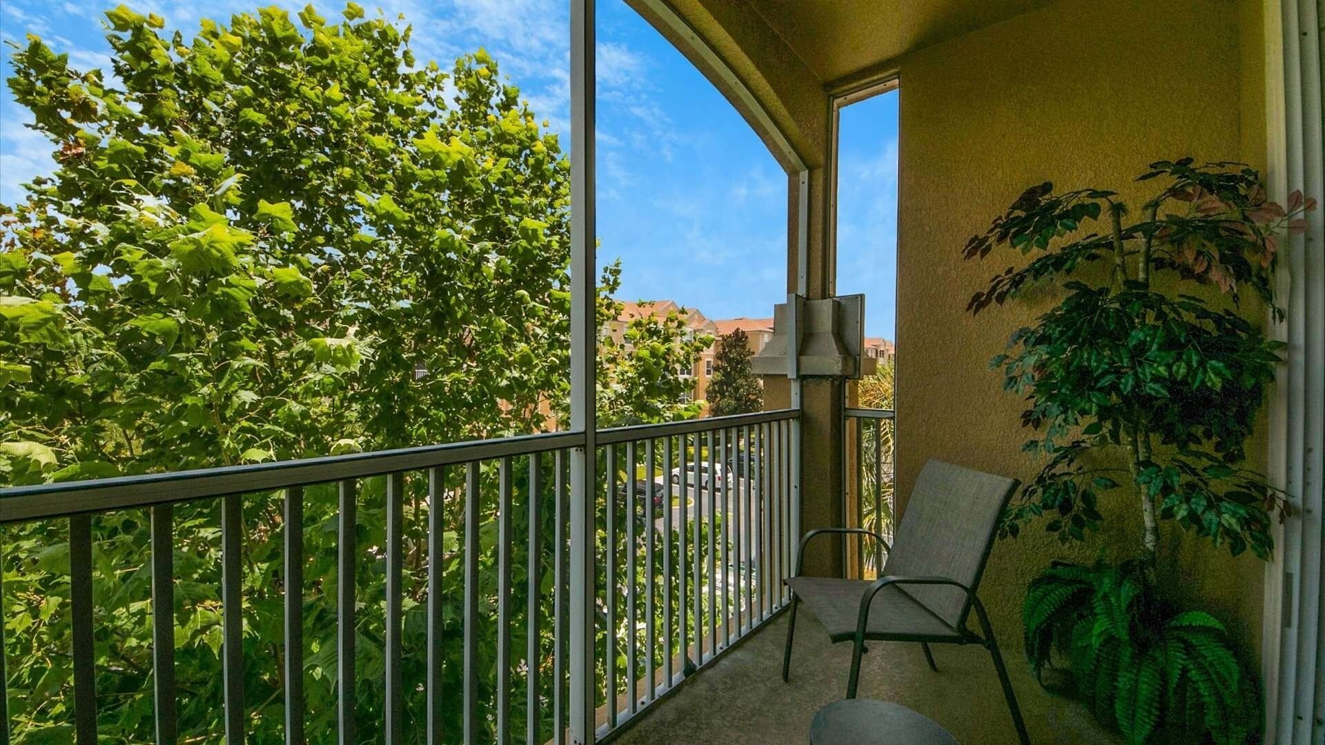 A balcony with a chair, a potted plant, and a view of trees and buildings.