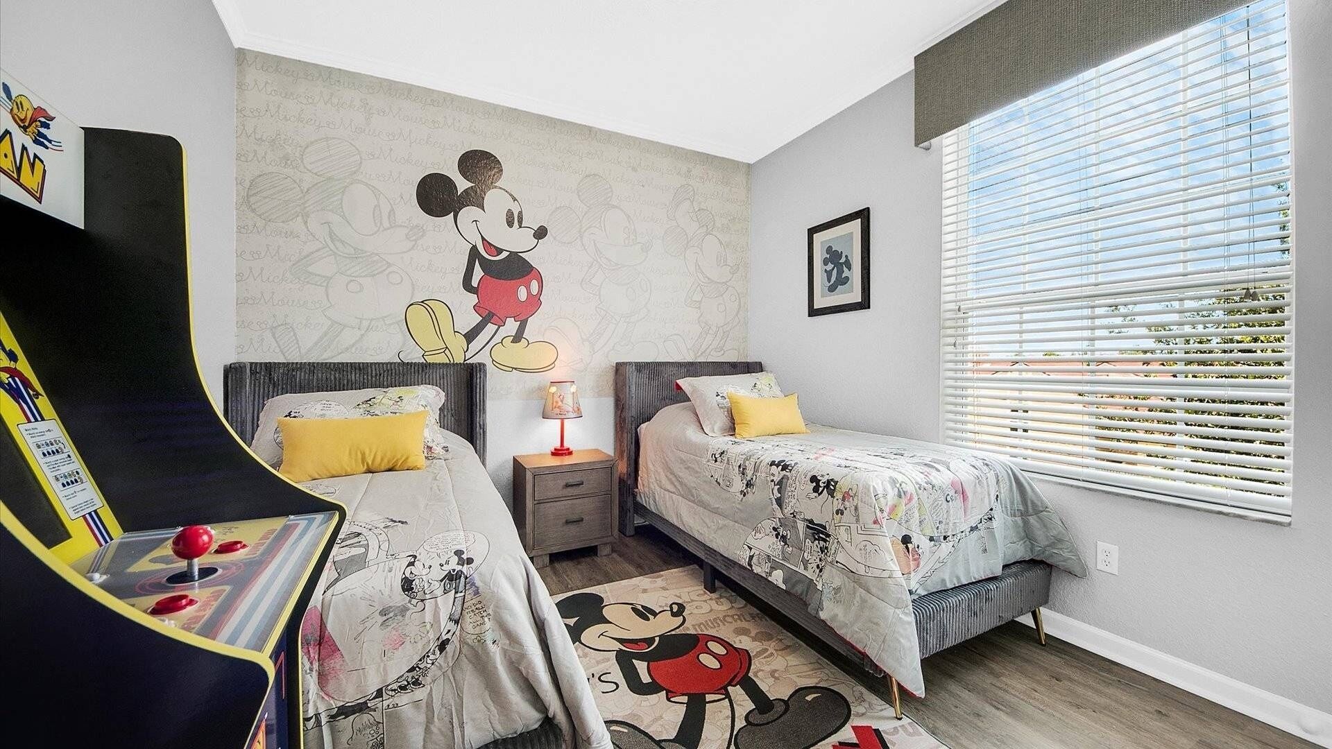 A bedroom with two beds, a Mickey Mouse mural, and a gaming console.