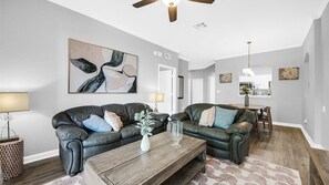 Ein Wohnzimmer mit zwei Ledersofas, einem Holztisch und einem Deckenventilator.