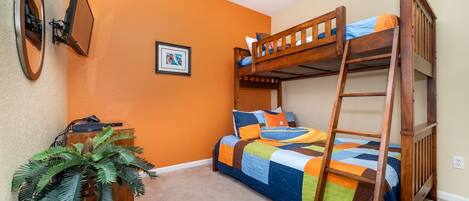 A room with a bunk bed, a desk with a computer, a framed picture on the wall, and a potted plant.