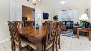 A dining area with a wooden table and chairs, a TV mounted on the wall, and a living room with a sofa and a lamp. - Windsor Hills Resort 3 Bedroom 2nd Floor Condo with Resort Access 3 Condo (Kissimmee)