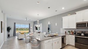 A modern kitchen with white cabinetry, a central island, stainless steel appliances, and a view to the outside.