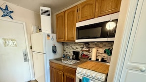 Une cuisine de taille réduite, dotée de meubles en bois, d’un réfrigérateur blanc, d’une cuisinière et d’un four à micro-ondes.