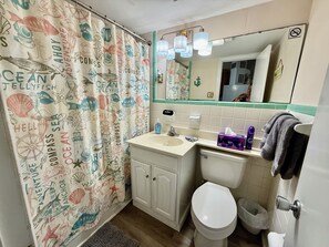 Een badkamer met een douchegordijn met nautisch thema, een wastafel, een toilet en een spiegel boven de wastafel.