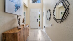 A hallway with a wooden cabinet, a large abstract painting, and geometric wall mirrors. - Windsor Hills Resort 5 Bedroom Private Pool Home 5 Home (Kissimmee)