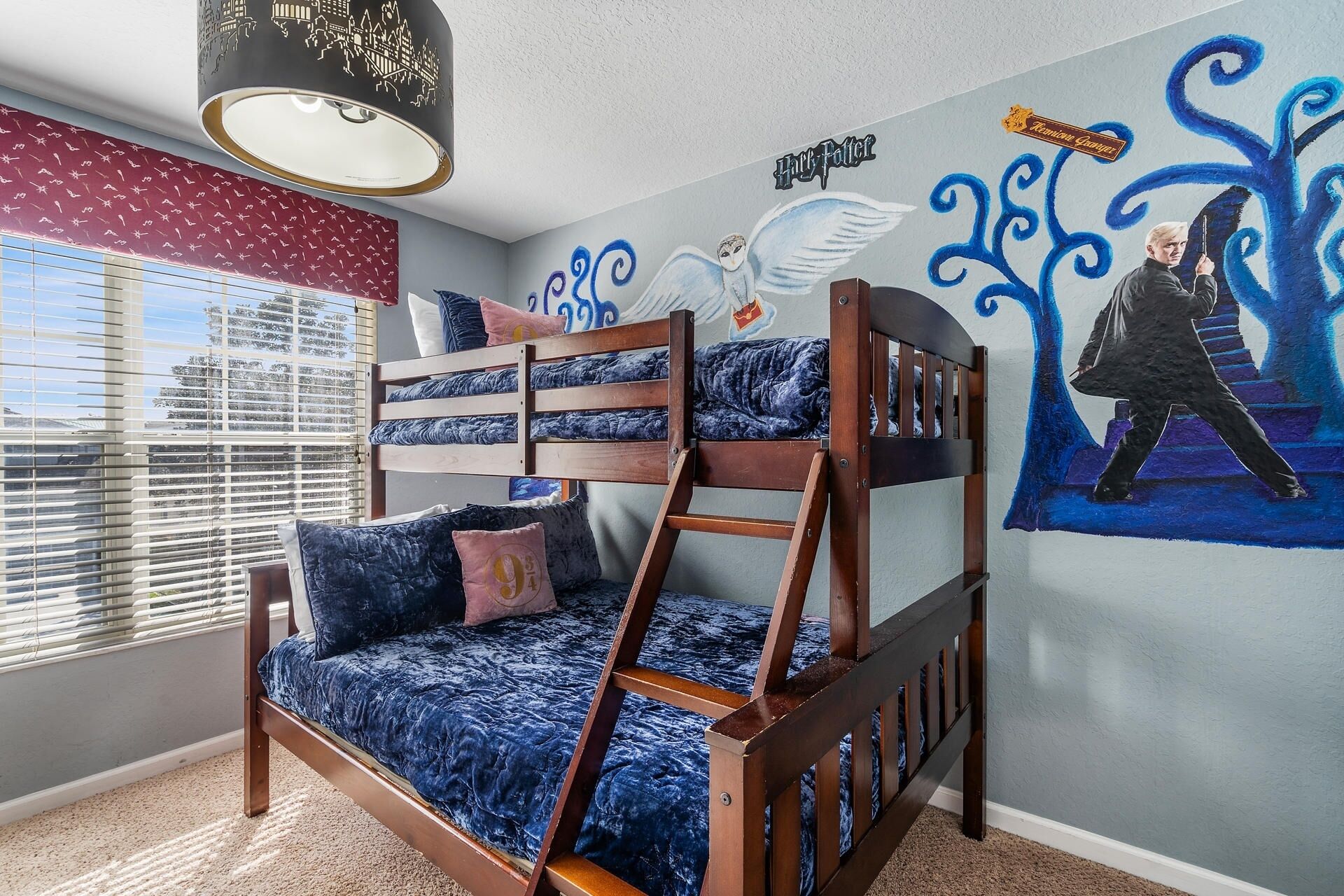 Une chambre d’enfant avec des lits superposés, une fenêtre avec des stores et une fresque murale.
