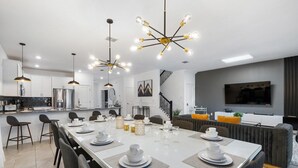 Eine moderne Küche mit weißen Schränken, einem Edelstahlkühlschrank und einem Essbereich mit einem langen Tisch, gedeckt für sechs Personen.