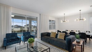 Ein modernes Wohnzimmer mit einer Couch, Sesseln, einem Glastisch und einem Essbereich mit Tisch und Stühlen.