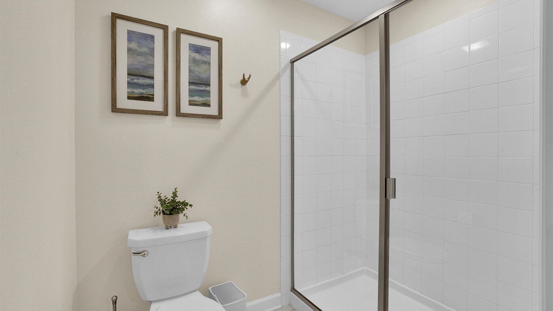Un baño con inodoro, ducha con puerta de cristal y dos cuadros en la pared.