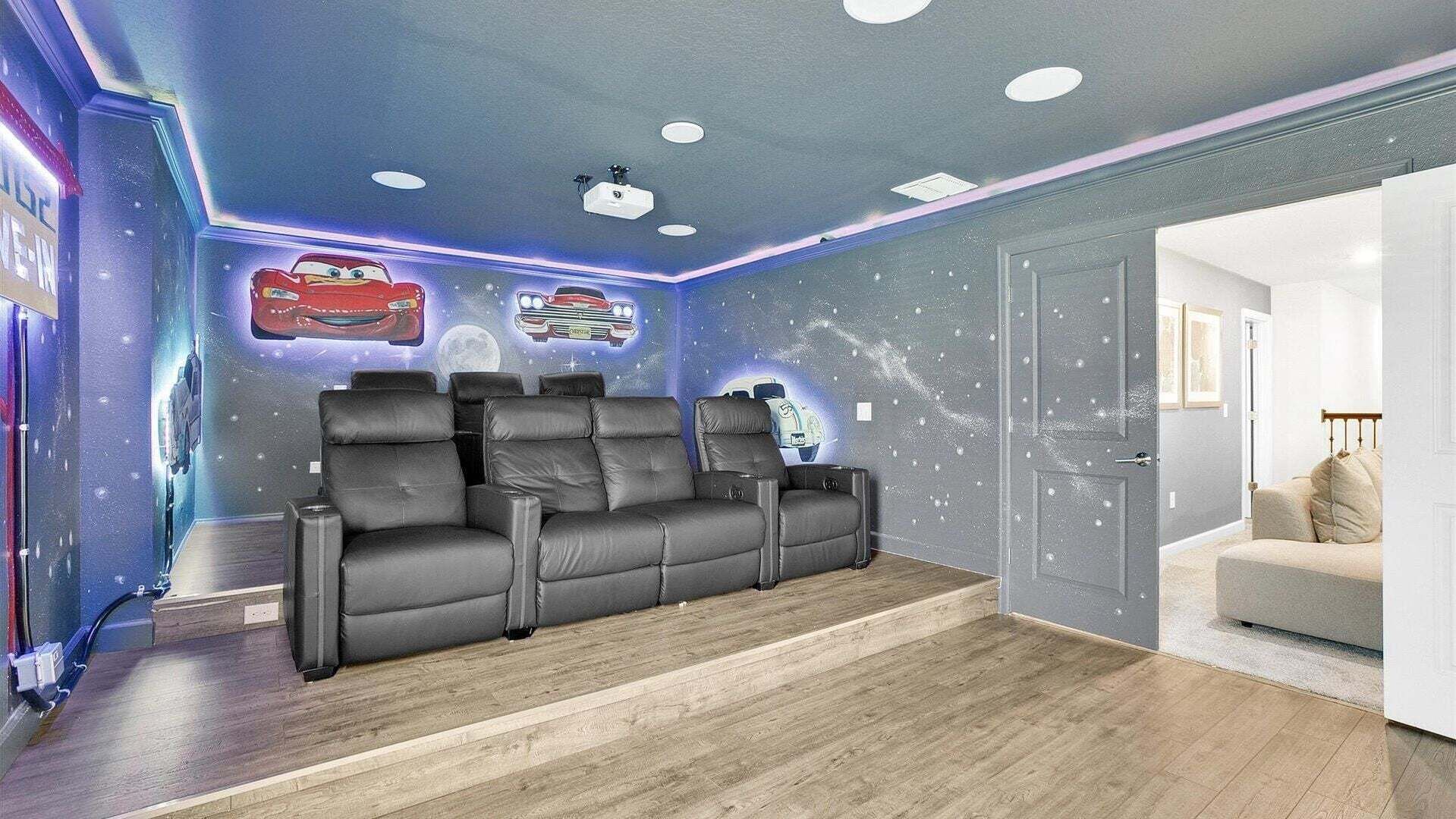 A home theater room with a reclining sectional sofa, a ceiling with recessed lighting, and a wall with a space-themed mural.