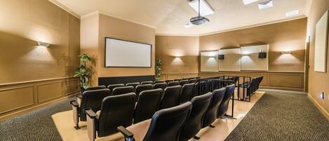 A conference room with rows of chairs, a large screen, and a projector.