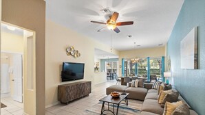 A spacious living room with a large flat-screen TV, a ceiling fan, and a dining area with natural light. - Windsor Hills Resort 4 Bedroom Home with Pool+Spa 4 Home (Kissimmee)