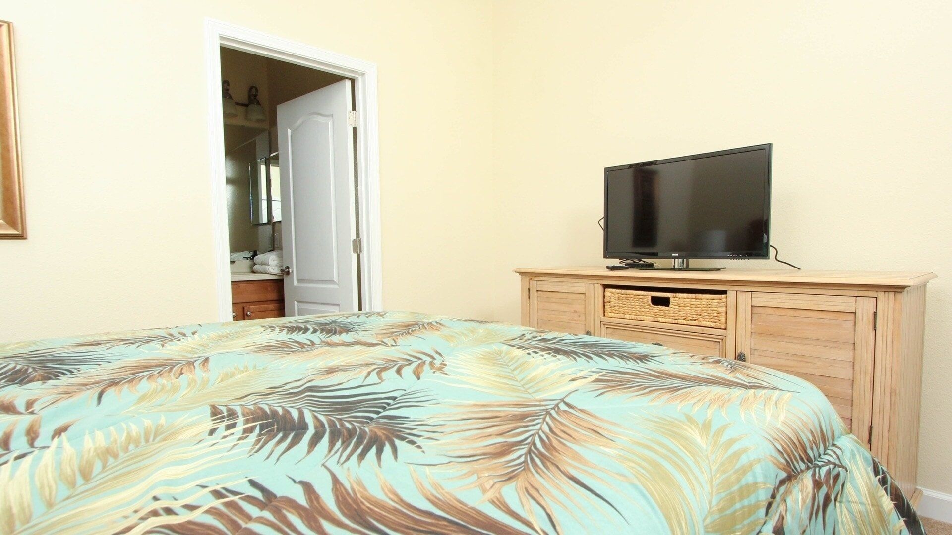 Une chambre à coucher avec un lit, un téléviseur posé sur un meuble en bois et une porte donnant sur une salle de bain.